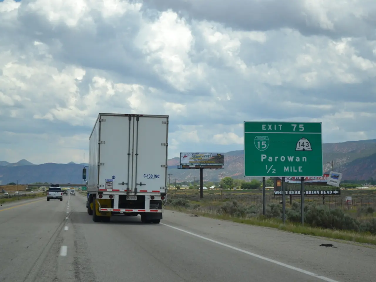 In this image we can see motor vehicles on the road, advertisement boards, sign boards, grass,...