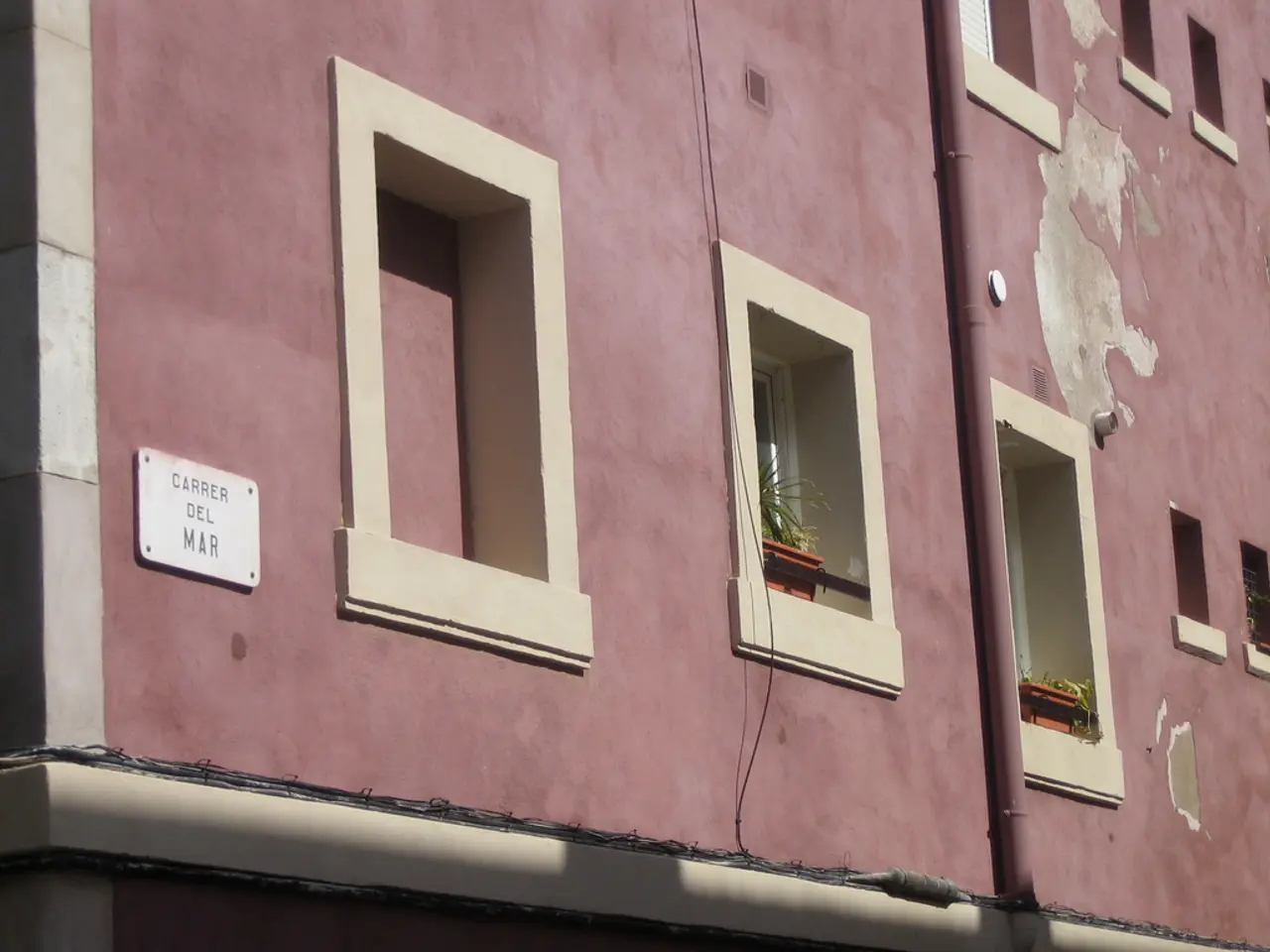 In this image there is a building with name plate, pipes, on the building there are flower pots on...