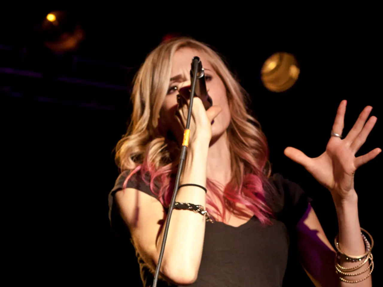 This is a picture of a woman standing and singing a song by holding a microphone and the back...