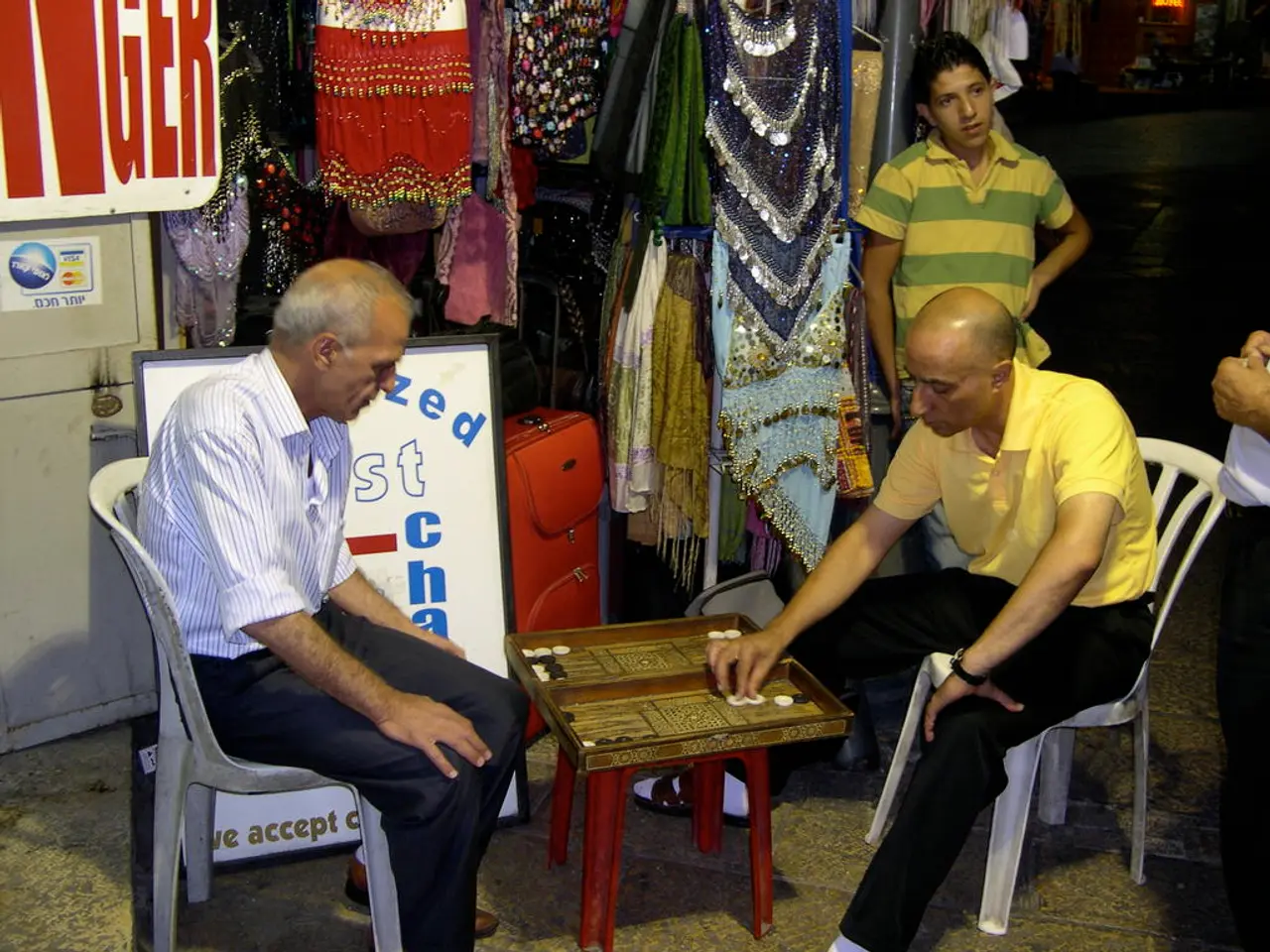 In this image we can see two men are sitting on the chair and playing a board game which is on the...