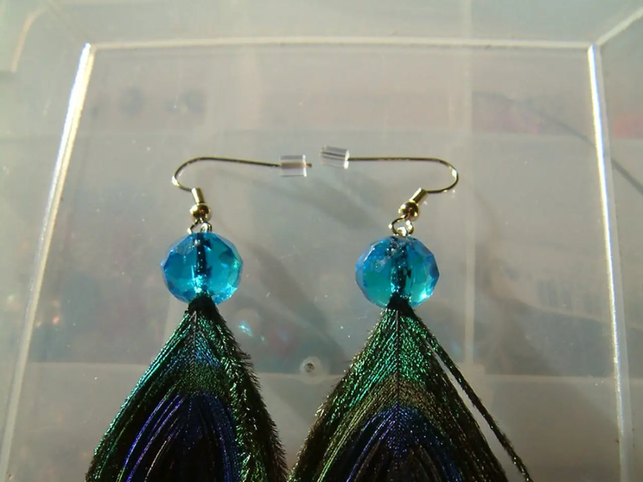 In this picture we can see the pair of green color peacock feather earring, placed on the plastic...