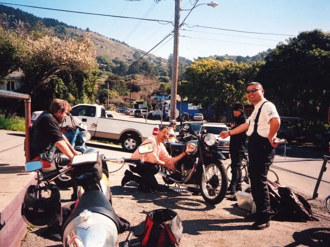 in this picture we see few men with the motor cycles and few cars parked along and we see some...