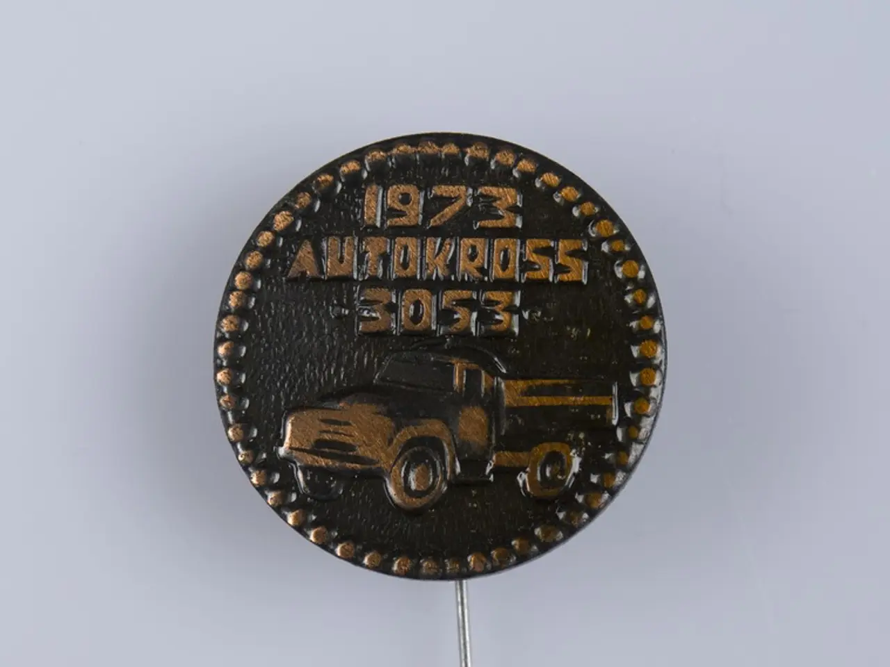 The image shows a black and gold button with a picture of a truck on it, set against a white...