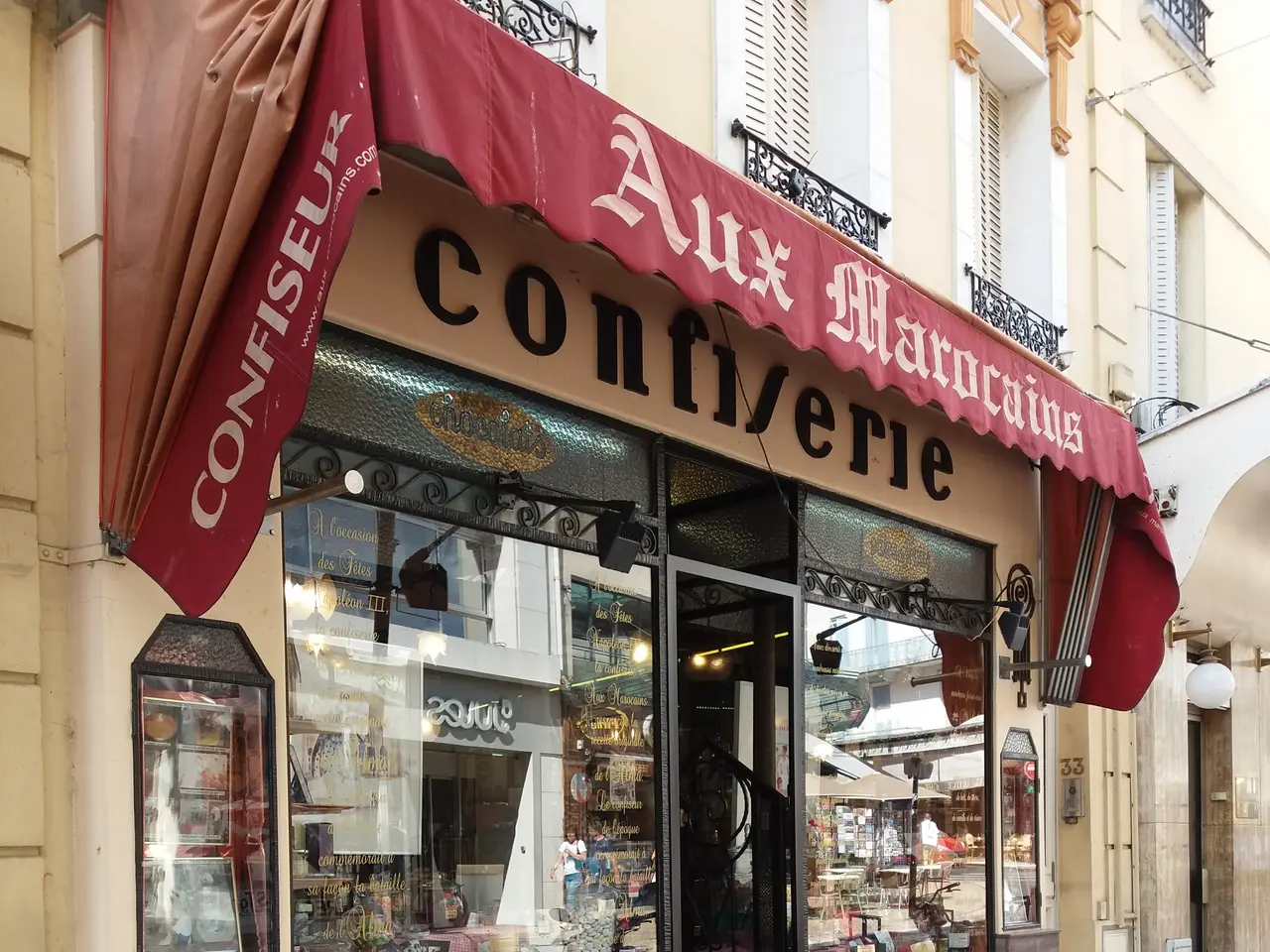 The image shows a store front with a red awning on the side of it, surrounded by buildings with...