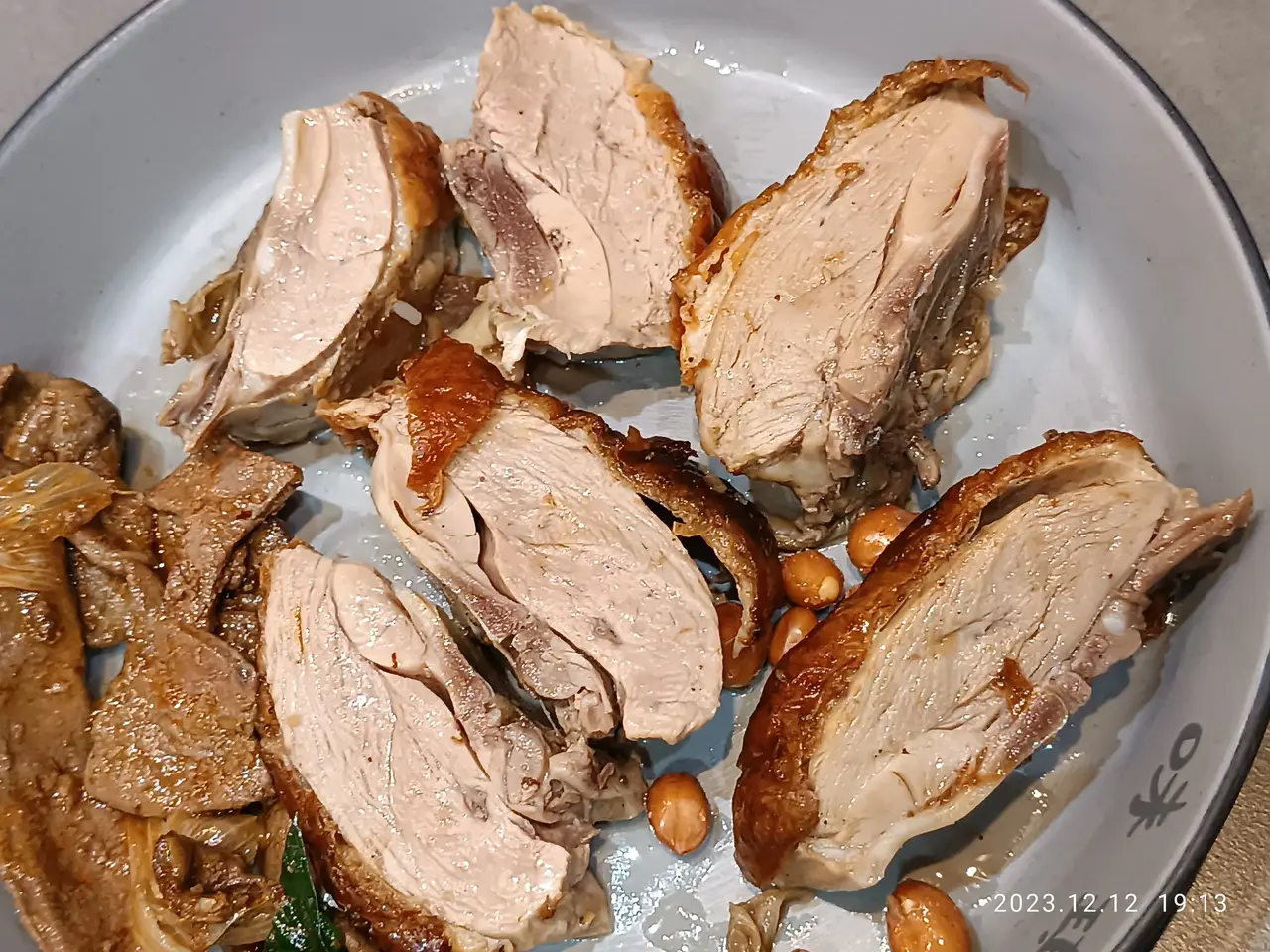 The image shows a white plate on a table, topped with sliced pork and peanuts. The pork is cooked...