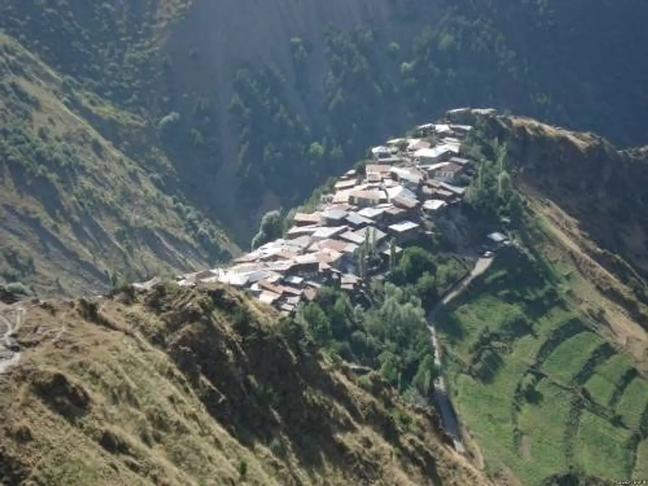 The image shows a small village nestled in the middle of a mountain, surrounded by lush green hills...
