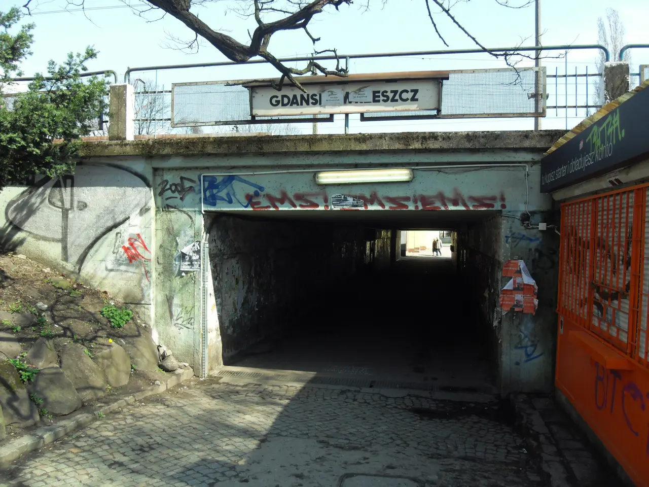 The image shows a tunnel with graffiti on the side of it, illuminated by a light at the top of the...