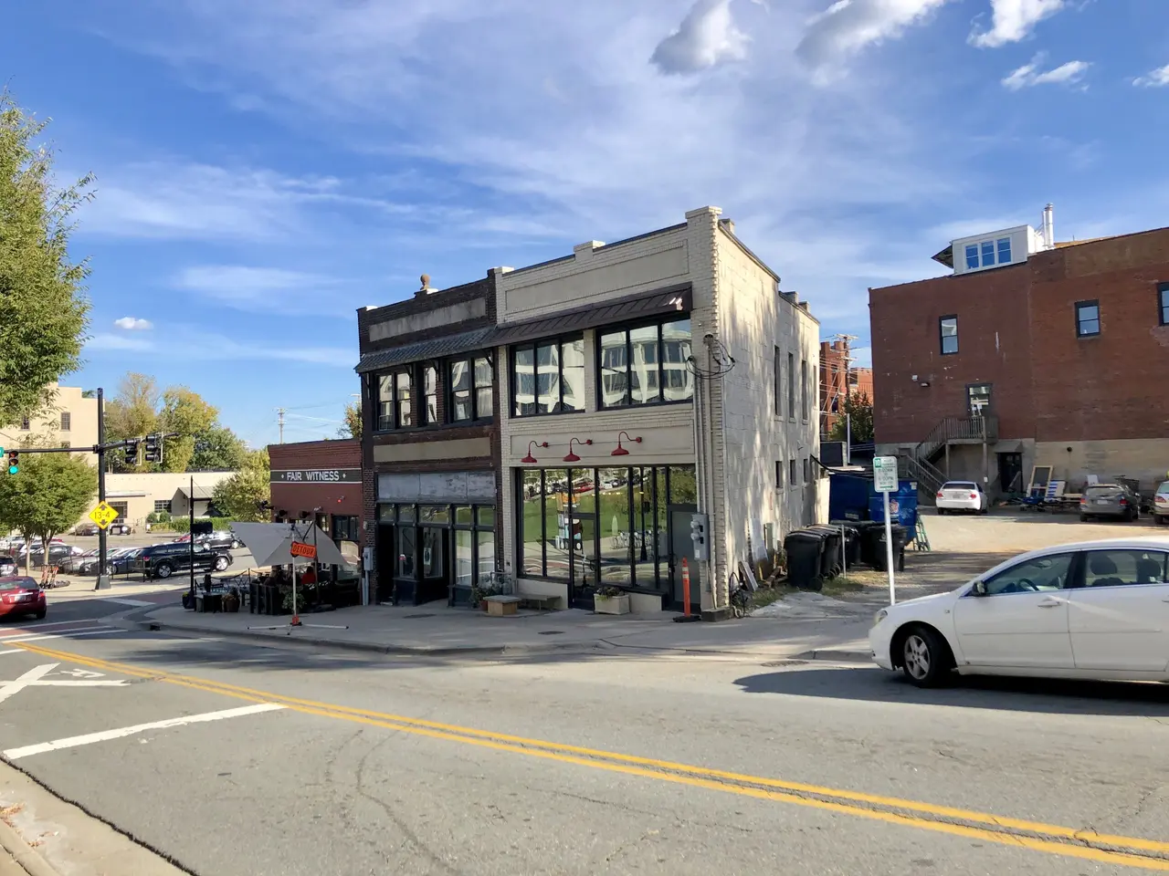 The image shows a city street with cars parked on the side of it, buildings with windows, light...