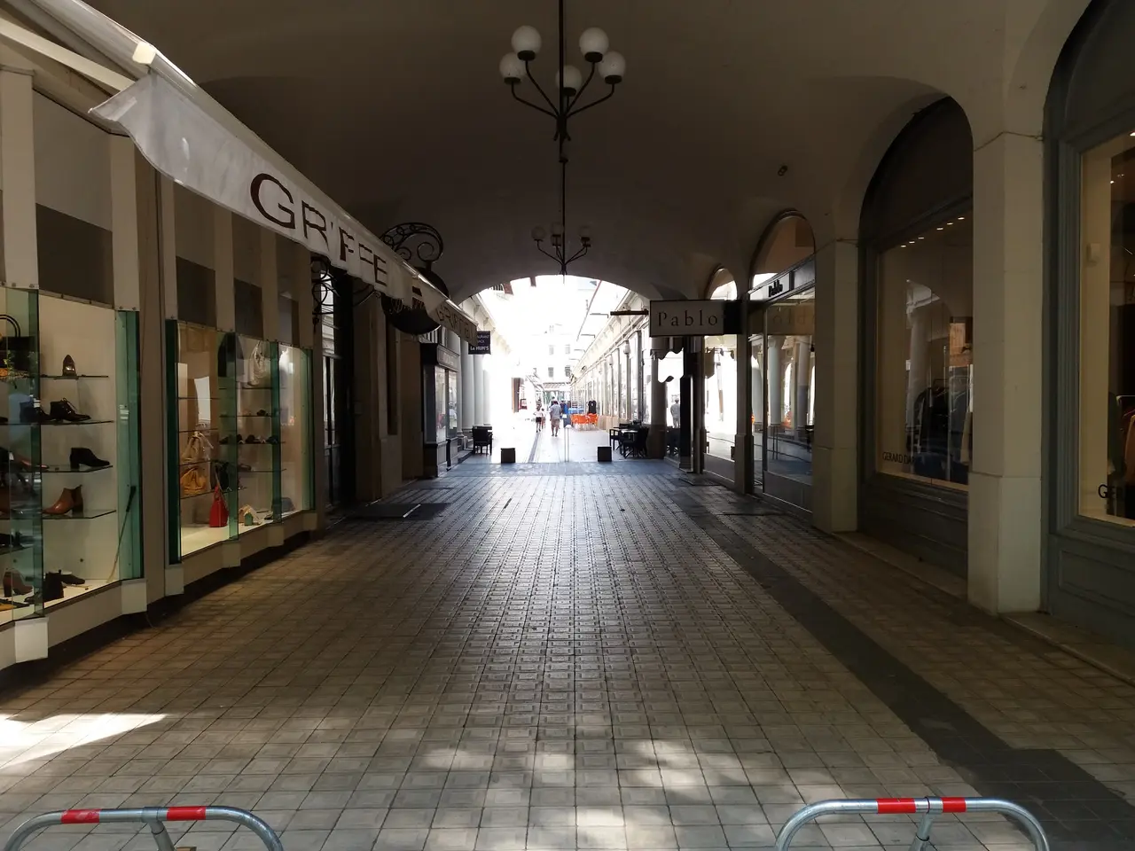 The image shows an empty shopping mall with people walking down it. On the left side of the image,...
