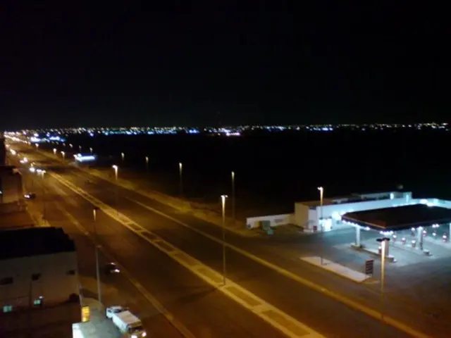 In this picture I can see the road and street lights. On the right I can see the darkness. In the...