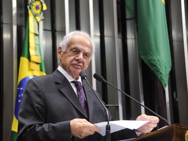 In this image there is a man standing. He is holding a paper in his hand. In front of him there is...