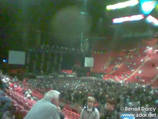 In this image we can see many people standing and sitting in the stadium. Here we can see LCD...