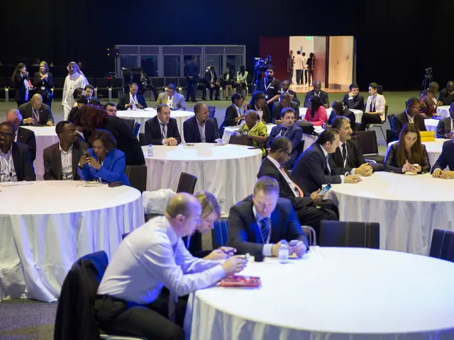 People are sitting in groups at tables. There are some people behind sitting separately.