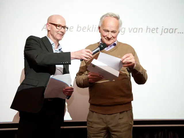 This is a screen behind these two men. They both are holding papers in their hands. This man wore...