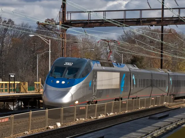 This picture contains a metro train moving on the railway track. Beside that, we see a fence and...