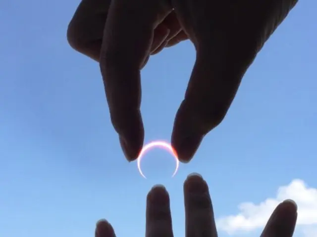 In this picture we can see a ring in a person's hand. There is another hand. Sky is blue in color...