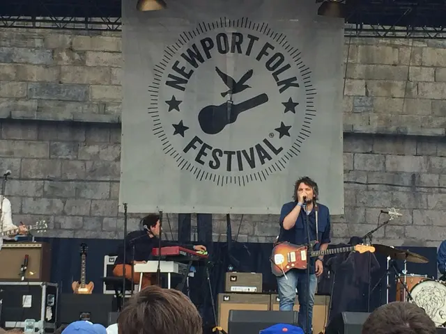 This image is clicked in a concert. There is banner in the middle of the image. And There are three...