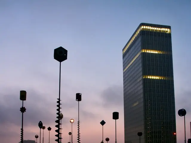 In this image I can see number of poles, number of buildings, lights, clouds and the sky in the...