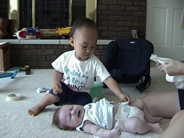 In this image on the ground there is a carpet. A baby is lying on the ground. The baby is crying....