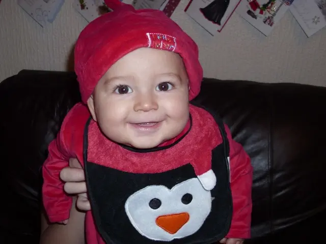 In the picture we can see a baby, child sitting on a sofa which is brown in color and child with...