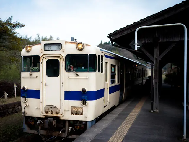 This picture shows a train on the railway track and we see a platform with a roof and we see a pole...