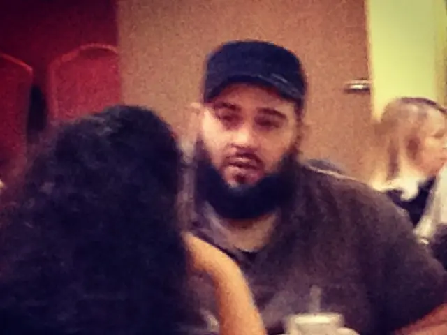 This picture shows few people seated. we see a man wore a cap on his head and few cups on the...