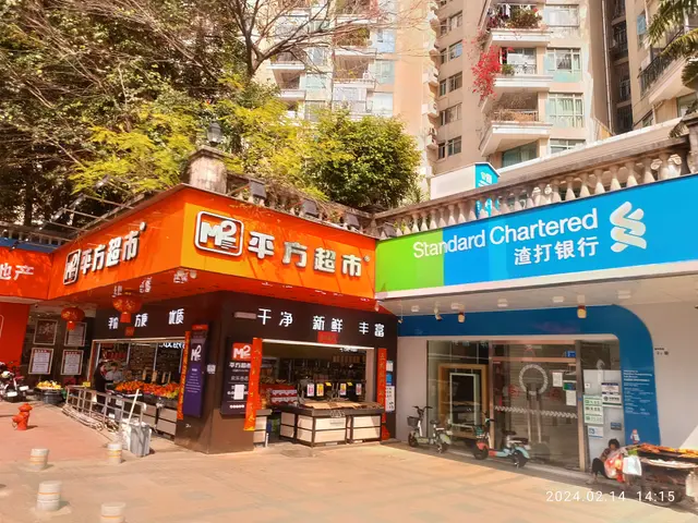 The image shows a standard chartered store in Hong Kong, with buildings, trees, motorbikes, people,...