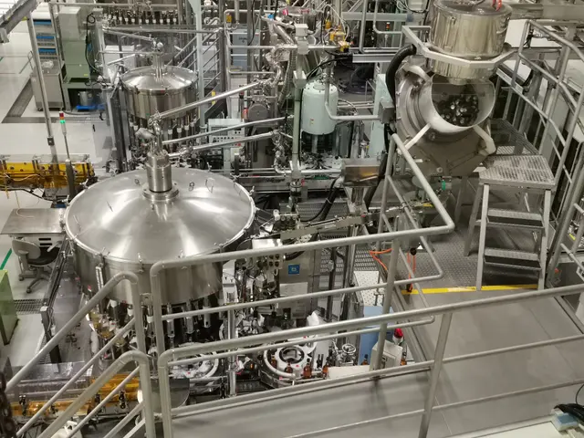 The image shows a large machine inside of a building, with a floor at the bottom, railings, stairs,...