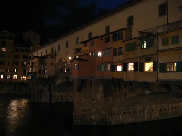 The image shows the Ponte Vecchio in Florence, Italy at night, illuminated by the lights of the...