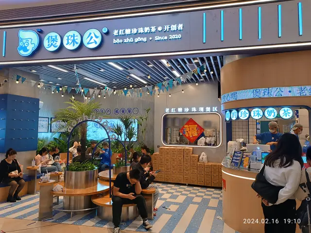The image shows a group of people sitting at tables in front of a store, with some of them holding...