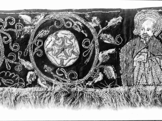 The image shows a black and white photo of a textile with intricate designs and text. The design is...