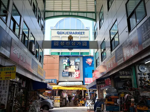 The image shows a bustling street filled with lots of shops and people walking down it. On either...