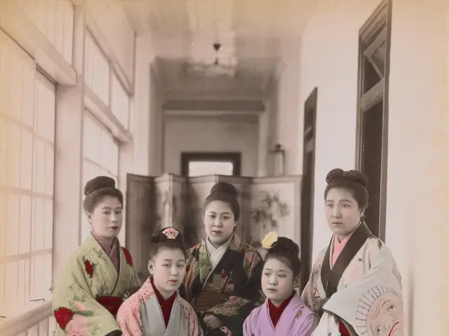 The image shows a group of five Japanese women in kimono posing for a photo in front of a wall with...