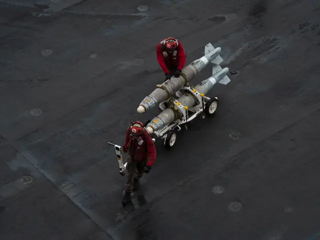 The image shows two men in red jackets and helmets standing on the deck of an aircraft carrier,...