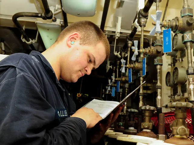 The image shows a man in a blue shirt standing in a boiler room, holding a book in his hands and...