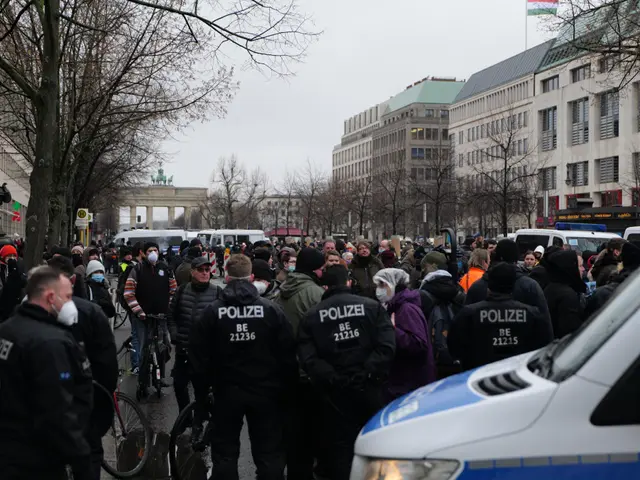 The image shows a large group of people standing in front of a police van on a road surrounded by...