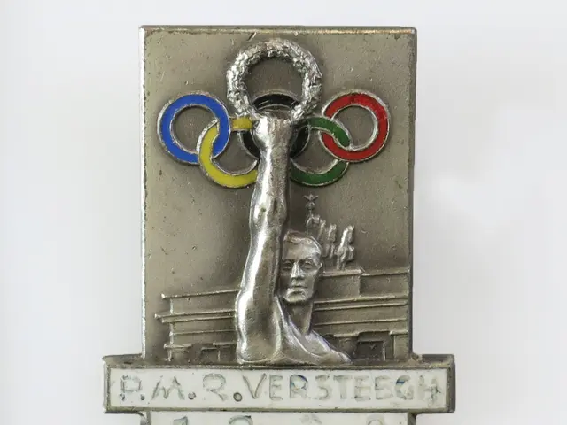 The image shows a silver medal with the Olympic rings on it, depicting a person holding the rings...