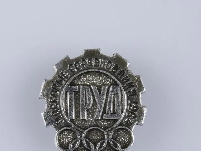 The image shows a silver badge with the words "Olympic Games" written on it against a white...
