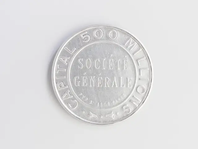 The image shows a silver coin on a white surface with the words "Capital 500 Millionaires" written...