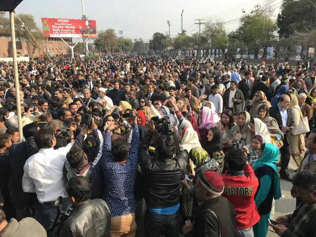 The image shows a large crowd of people standing in front of a building, with some of them holding...