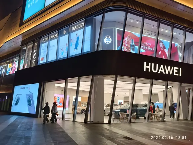 The image shows a Huawei store in Shanghai at night, illuminated by bright lights and surrounded by...