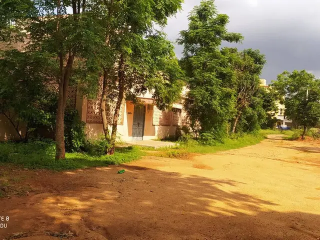 The image shows a residential plot for sale in Vijayawada, with buildings, trees, plants, grass,...