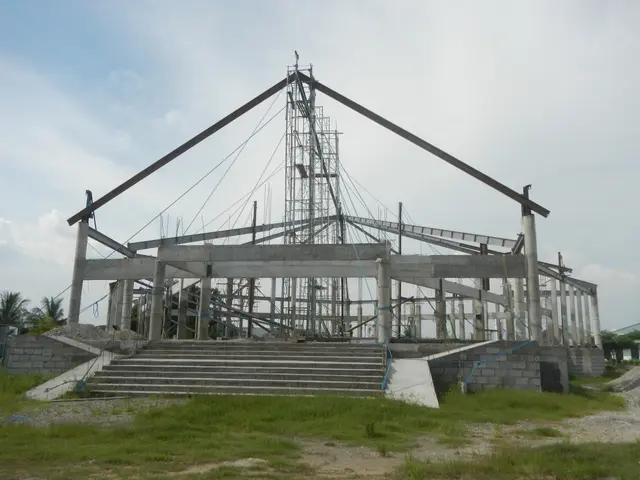 The image shows a large building under construction in the middle of a field, with stairs leading...