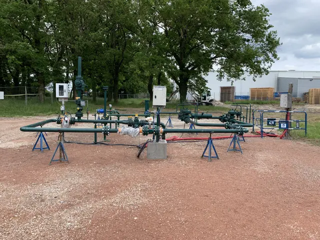 The image shows a large group of pipes and valves sitting on top of a dirt field surrounded by...