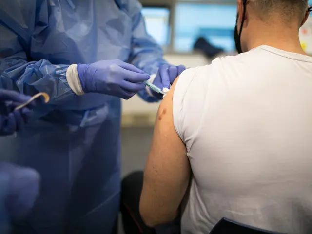 The image shows a man in a white shirt getting a vaccine from a doctor wearing a blue dress and...