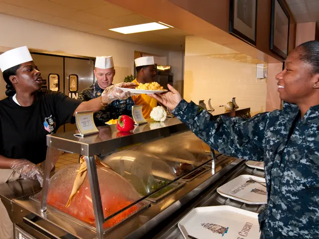 The image shows a woman in a military uniform serving food to a group of people wearing caps and...