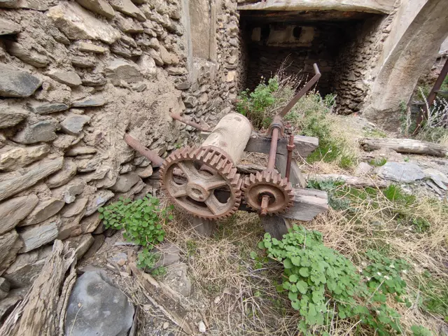The image shows an old rusty machine sitting in the middle of a stone wall, surrounded by grass,...