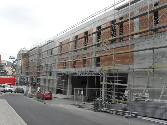 The image shows a large building under construction with scaffolding on the side of it, surrounded...