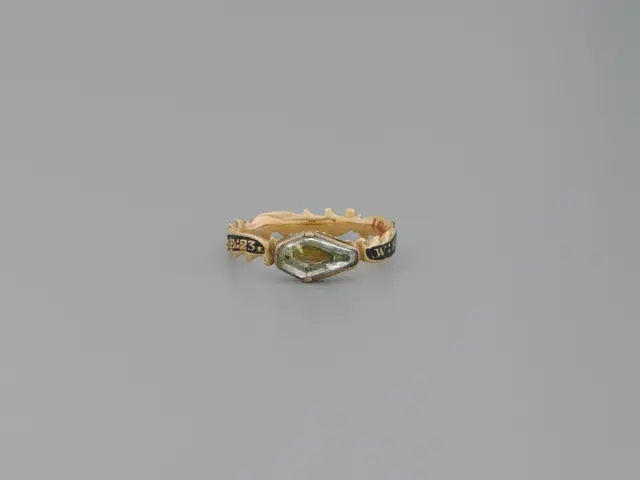 The image shows a gold ring with a marquis cut diamond in the center, surrounded by a halo of...