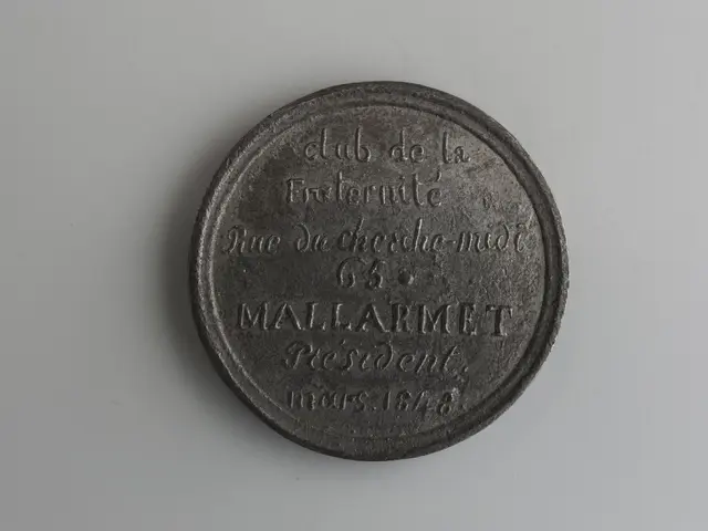 The image shows a black coin with text on it sitting on top of a white surface. The coin appears to...